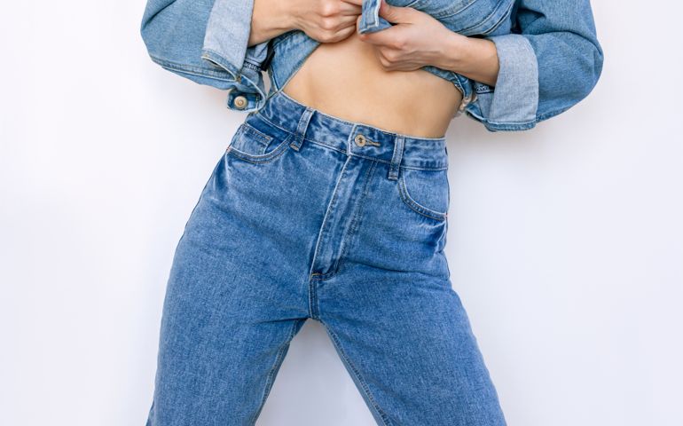 Cropped shot of young slender woman in fashionable blue jeans with a high fit on a white background