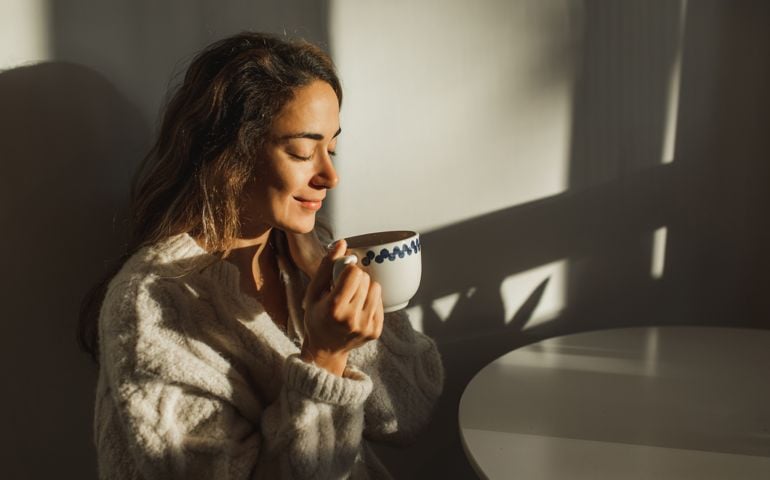 Young pretty woman enjoying morning coffee at home. Beautiful sun light in kitchen room.