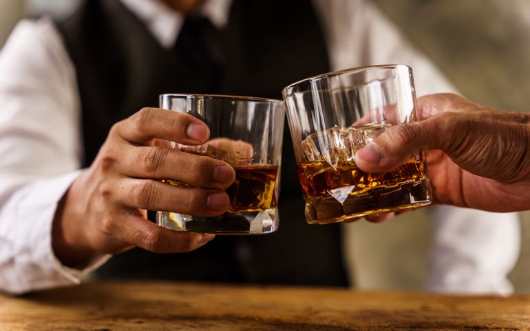 Two hands clink glasses of whiskey wiskey on the couch, cozy. Bar drinking menu.