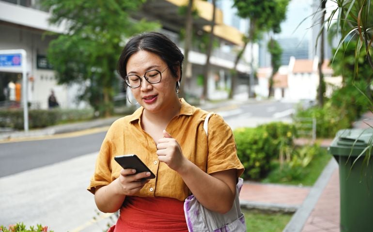 Asian woman waiting for a taxi along the street in Singapore with her phone