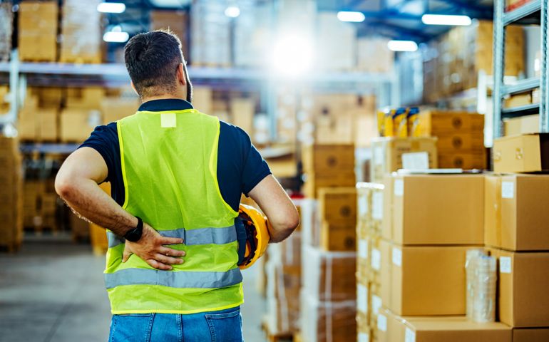 A warehouse worker having back pain and rubbing it.