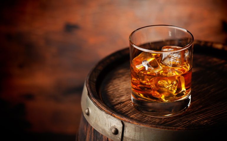 Glass of whiskey with ice cubes on the old barrel