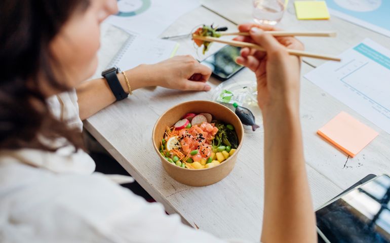 Businesswoman eating healthy poke bowl with chopsticks in lunch break at office