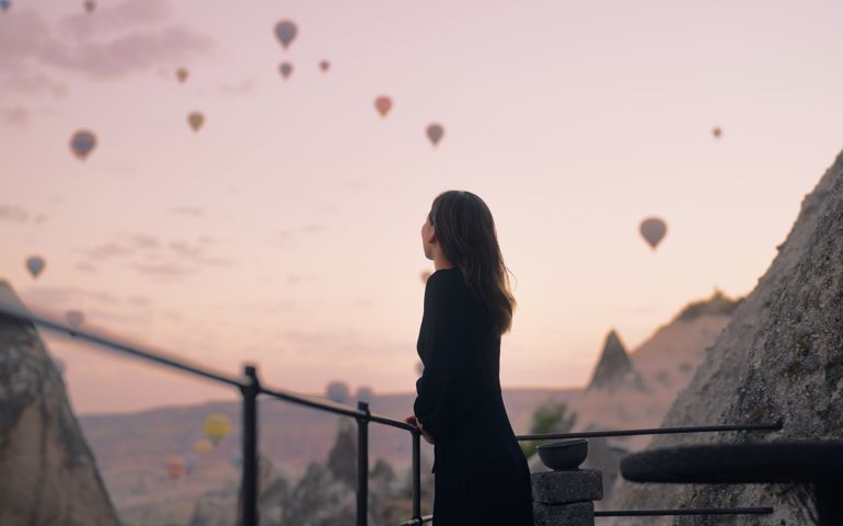 Female tourist enjoying watching hot air balloons flying in the sky at rooftop of hotel where she is staying during her vacation