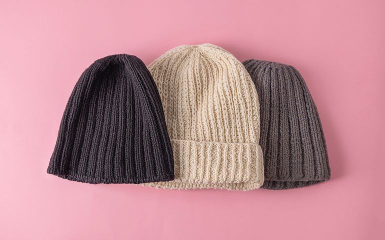 Top view of wool knitted hats on soft pink background. Handmade knitted clothes, winter close concept