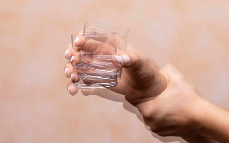 hand holding drinking glass suffering from Parkinson's disease