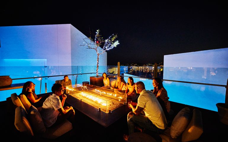 Wide shot of families relaxing around fire pit on rooftop at resort