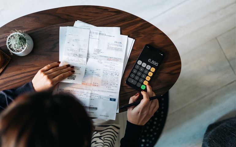 Overhead view of young Asian woman managing personal banking and finance at home. Planning budget and calculating expenses while checking her bills with calculator. Managing taxes and financial bills. Home budgeting. Concept of finance and economy