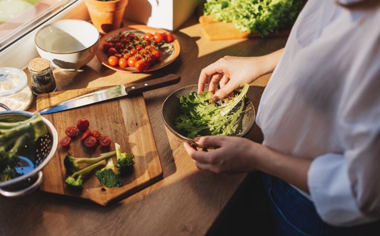 Healthy dinner or lunch. Woman in t-shirt and jeans standing and holding vegan superbowl or Buddha bowl with hummus, vegetable, salad, beans, couscous and avocado and smoothie in hands, square crop