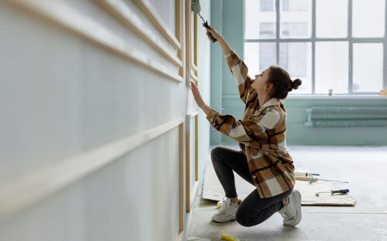 Young woman applying paint on wall in apartment
