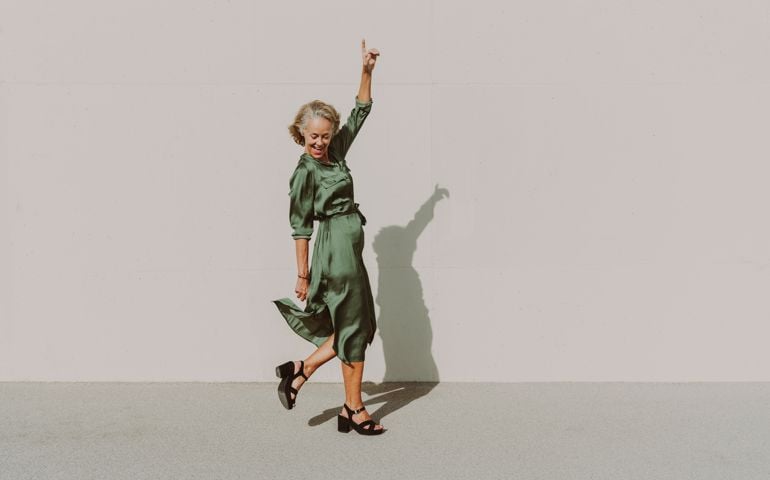 Happy woman dancing with hand raised on footpath
