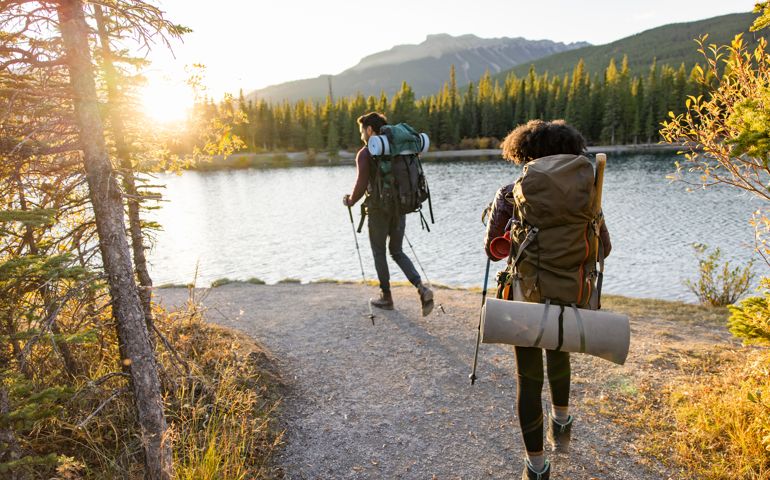Couple hiking on lakeside trail in sunny autumn woods at sunset