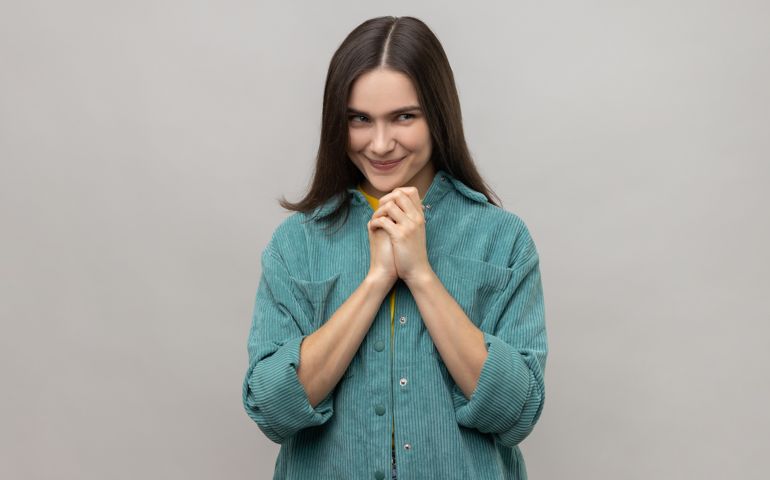 Devious cunning young woman with dark hair clasping hands and smirking mysteriously.