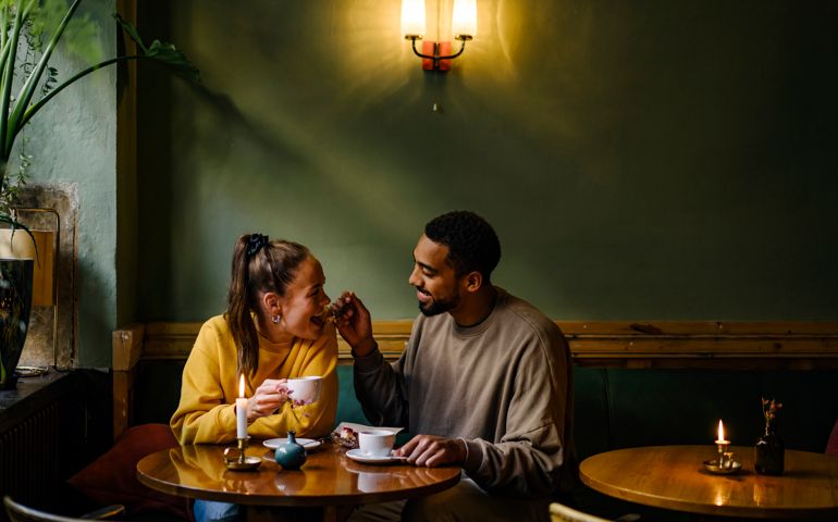 Wide shot of boyfriend feeding girlfriend a bite of dessert