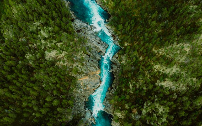 Scenic aerial view of the mountain landscape with a forest and the crystal blue river in Jotunheimen National Park