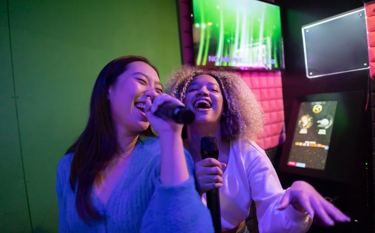 Happy young friends singing karaoke in microphone at amusement arcade