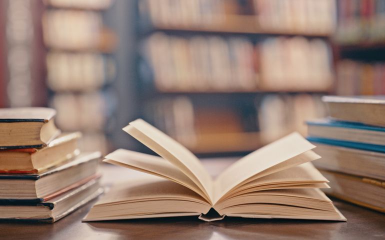 Library, books on table and background for studying, learning and research in education, school or college. Reading, philosophy and open, vintage or history print book, university blurred background