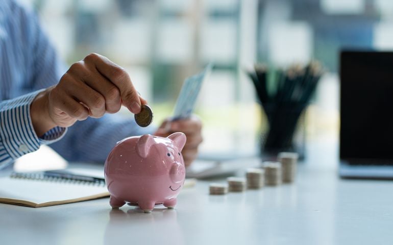 Hands of a young Asian businessman Man putting coins into piggy bank and holding money side by side to save expenses A savings plan that provides enough of his income for payments.