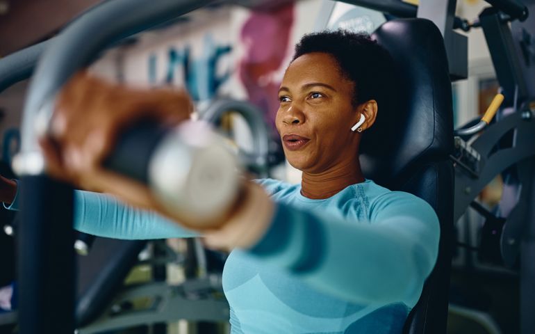 Black sportswoman doing chest exercises on machine while working out in gym.