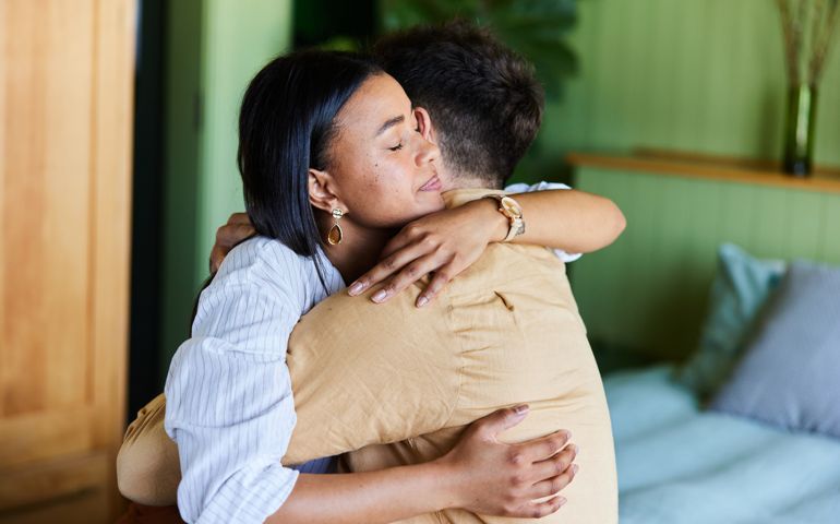 Loving woman hugging her upset husband in their bedroom at home