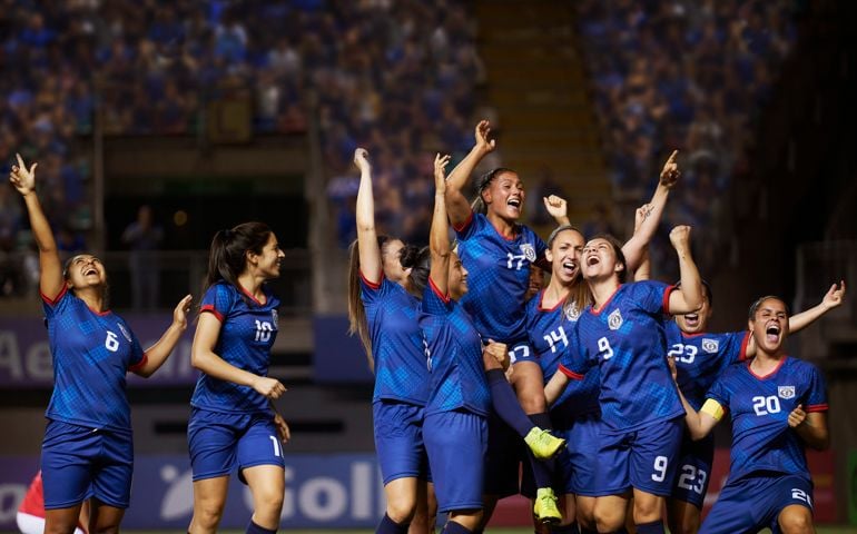 A team of female soccer players joyously react to a play during a sports competition.