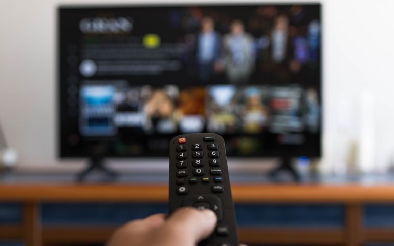 Hand holding remote control while searching for a series on television