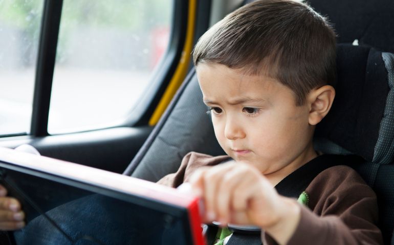 A japenese-american boy, a 4 year old boy, draws on his etch and sketch while sitting in his car seat.