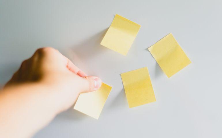 Hand is pinning or detaching a yellow sticky. Yellow note on fridge