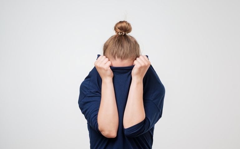 European woman hiding face under the clothes. She is pulling sweater on her head