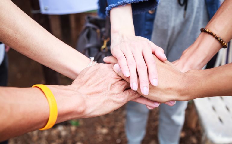 young men and women standing and stacking hands in a meeting on natural ground background at outdoor outing.