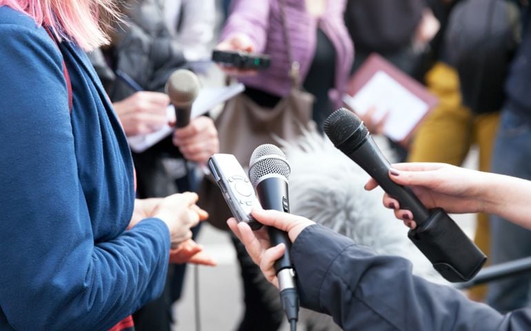 Public figure talking to the media, reporters holding microphones at news conference
