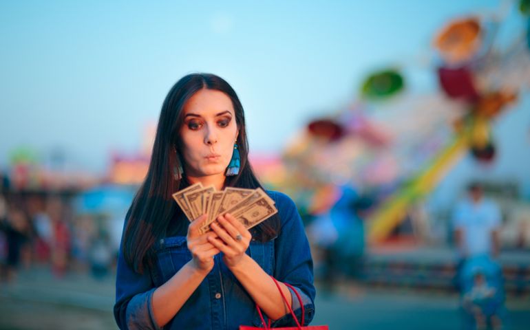 Woman Holding Cash Money at Summer Funfair. Millennial holding banknotes after lucky win in amusement park games
