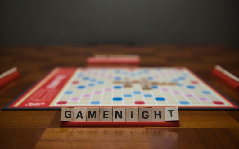 Letter tiles spelling out the words game night on stand in the foreground with out of focus game board in the background.