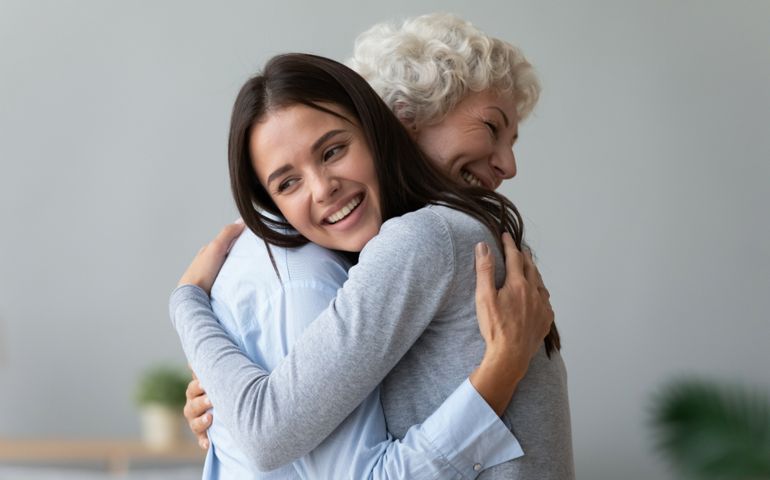 Happy young lady adult daughter granddaughter visiting embracing hugging old senior retired grandmother cuddling bonding, two age generations women expressing love and care at reunion meeting