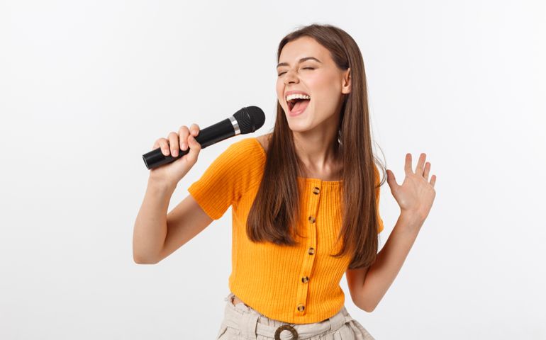 Young pretty woman happy and motivated, singing a song with a microphone, presenting an event or having a party, enjoy the moment