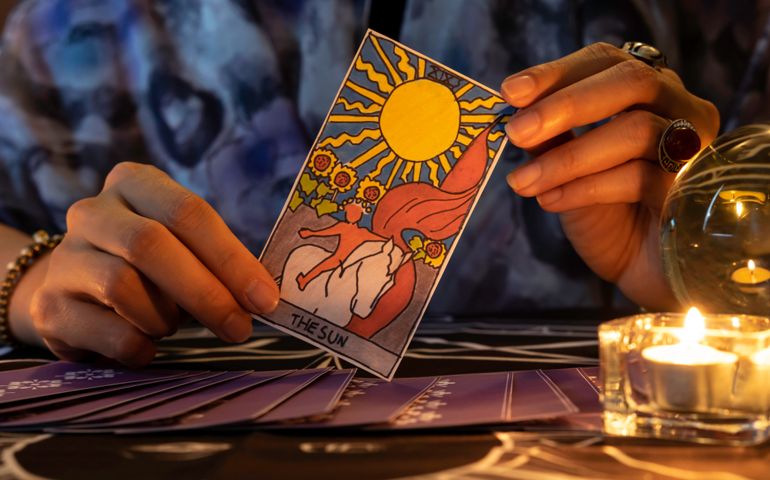 Fortune teller of hands holding THE SUN card and tarot cards on table near burning candles in candle light.Tarot cards spread on table with crystal ball.Forecasting concept.