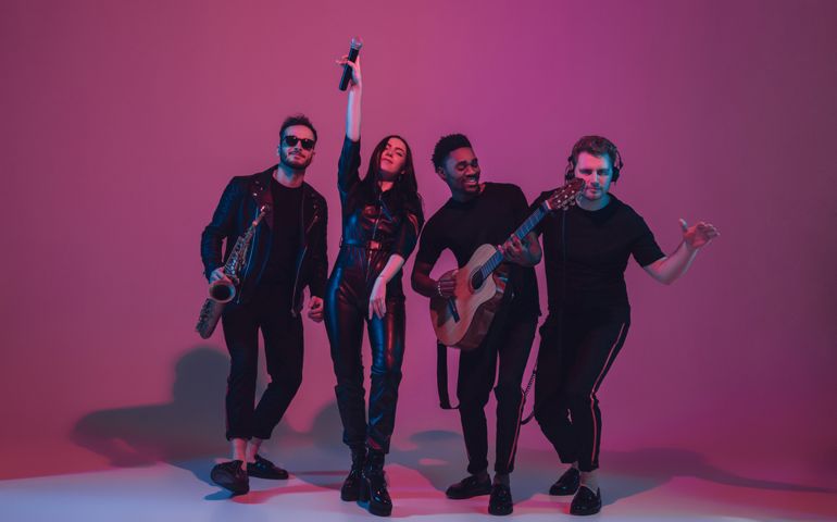 Group of young multiethnic musicians created band, dancing in neon light on pink background. Concept of music, hobby, festival, wellness. Joyful party host, dancer, singer, guitarist, saxophonist.