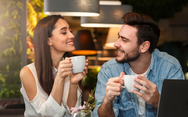 Dating. Young couple tasting coffee drinks enjoying flirt and conversation during weekend date sitting in cozy cafe