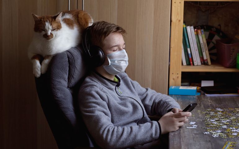 A teenager plays a game on the phone while sitting in a chair at a table. Concept quarantine and self-isolation. Healthcare and medical concept. Pandemic virus COVID-19