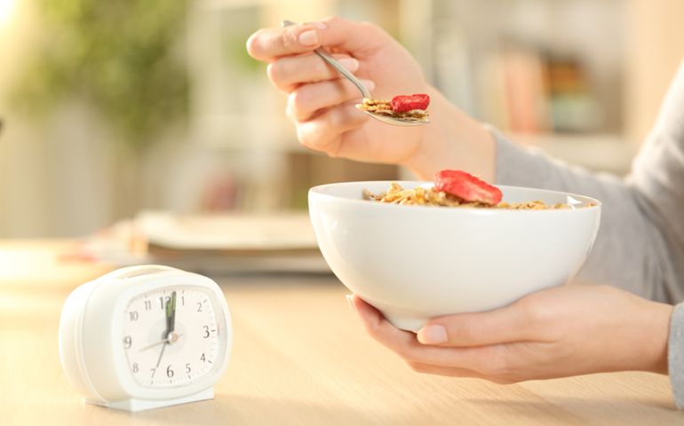 Close up of woman hands eating cereal bowl with fruit after intermittent fasting sitting on a table at home