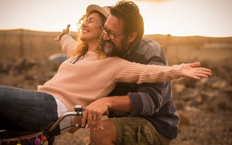 Happy adult people cheerful couple enjoy the outdoor leisure activity riding a bike together man carrying woman and laugh a lot in friendship and relationship - active youthful persons