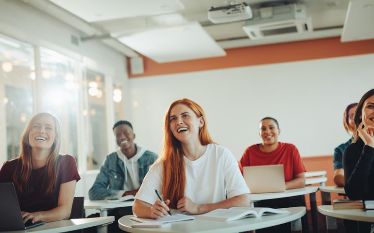 Group of teenage students smiling during the lecture in classroom. University students laughing in classroom.