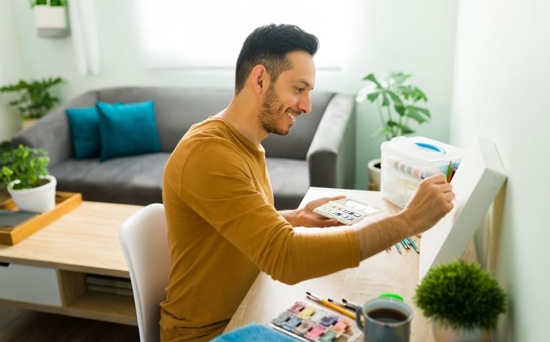 Happy man in his 30s doing a watercolor painting at home. Good-looking man smiling while relaxing with a wellness hobby