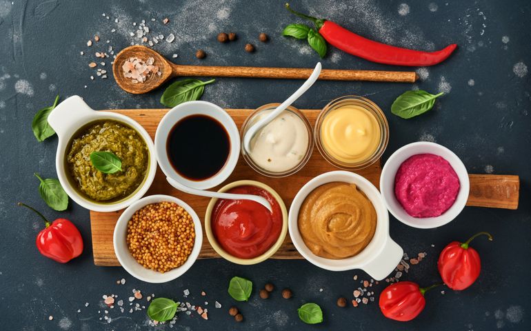 Set of sauces in bowls - ketchup, mayonnaise, mustard, soy sauce, bbq sauce, pesto, chimichurri, mustard grains on dark stone background.