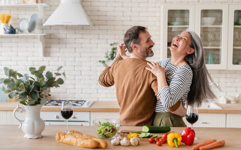 Happy cheerful middle-aged mature couple family parents dancing together in the kitchen, preparing cooking food meal for romantic dinner, spending time together. Active seniors