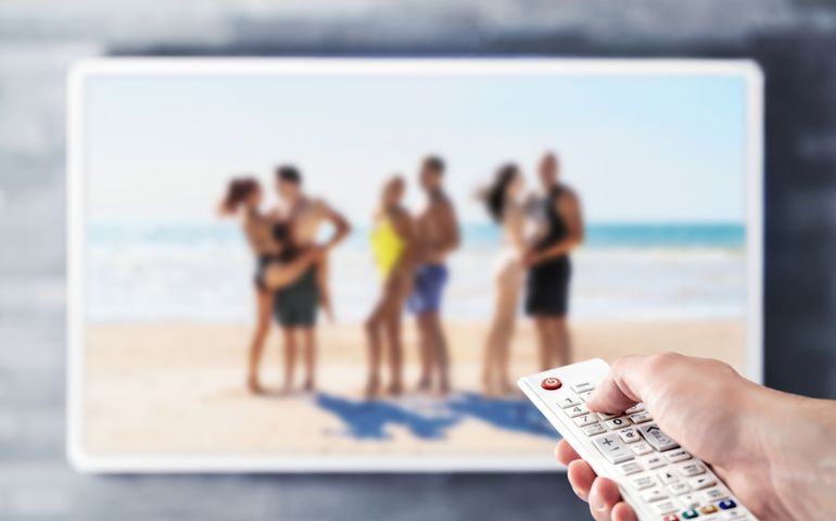 Reality tv show stream on television. Watching series on VOD streaming service. Couples at the beach or island dating, looking for love. Person using remote control. Contest or celebrity entertainment