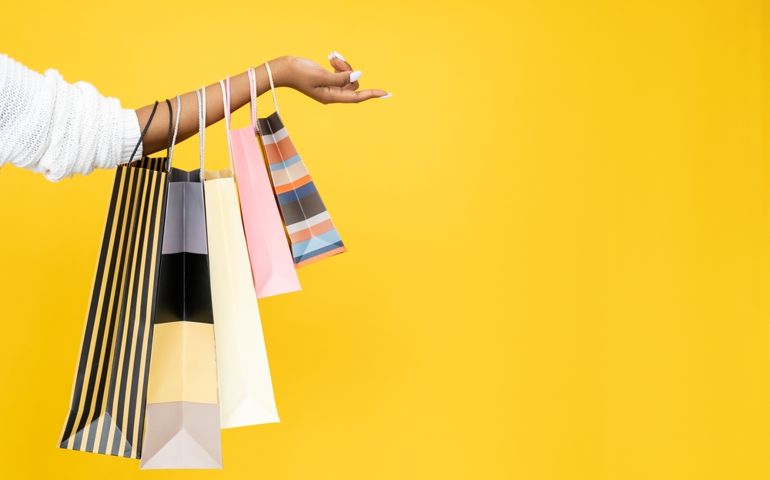 Sale offer. Black Friday. Shopping discount. Closeup of Afro woman hand holding purchase bags isolated on orange empty space background.