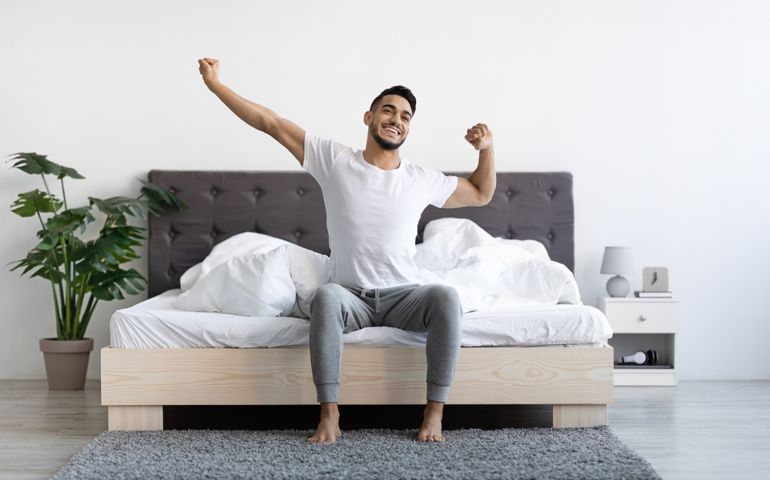 Handsome Happy Young Arab Guy Waking Up In The Morning, Sitting On Bed And Stretching After Good Sleep, Smiling Millennial Middle Eastern Man Having Good Mood, Enjoying Start Of New Day, Copy Space
