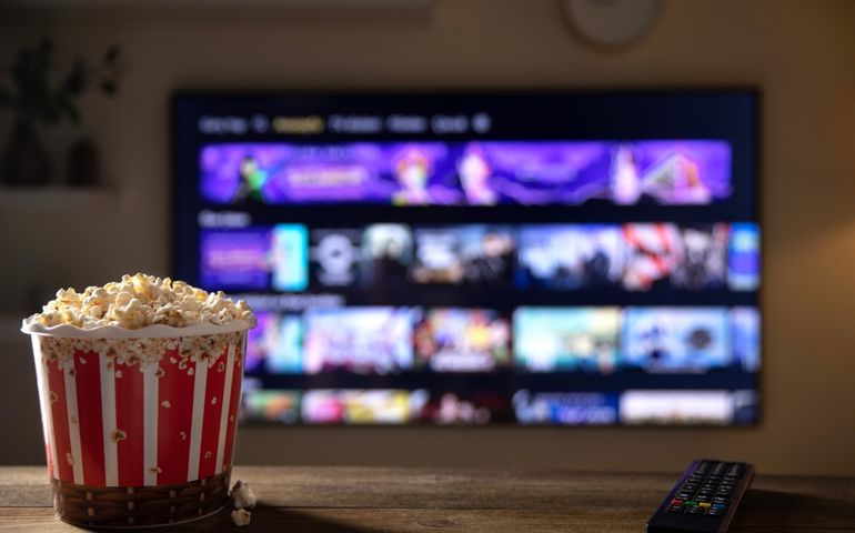 Close up of bowl of popcorn and remote control with tv works on background. Evening cozy watching a movie or TV series at home.