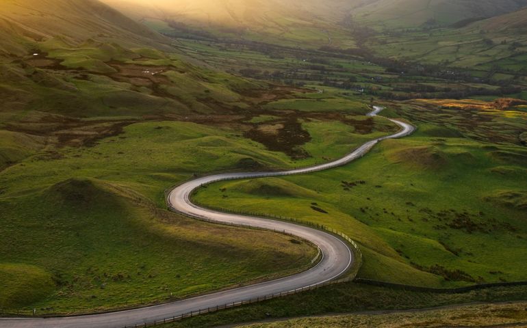Long winding road in British rural countryside leading off into distance. Peak District, UK.